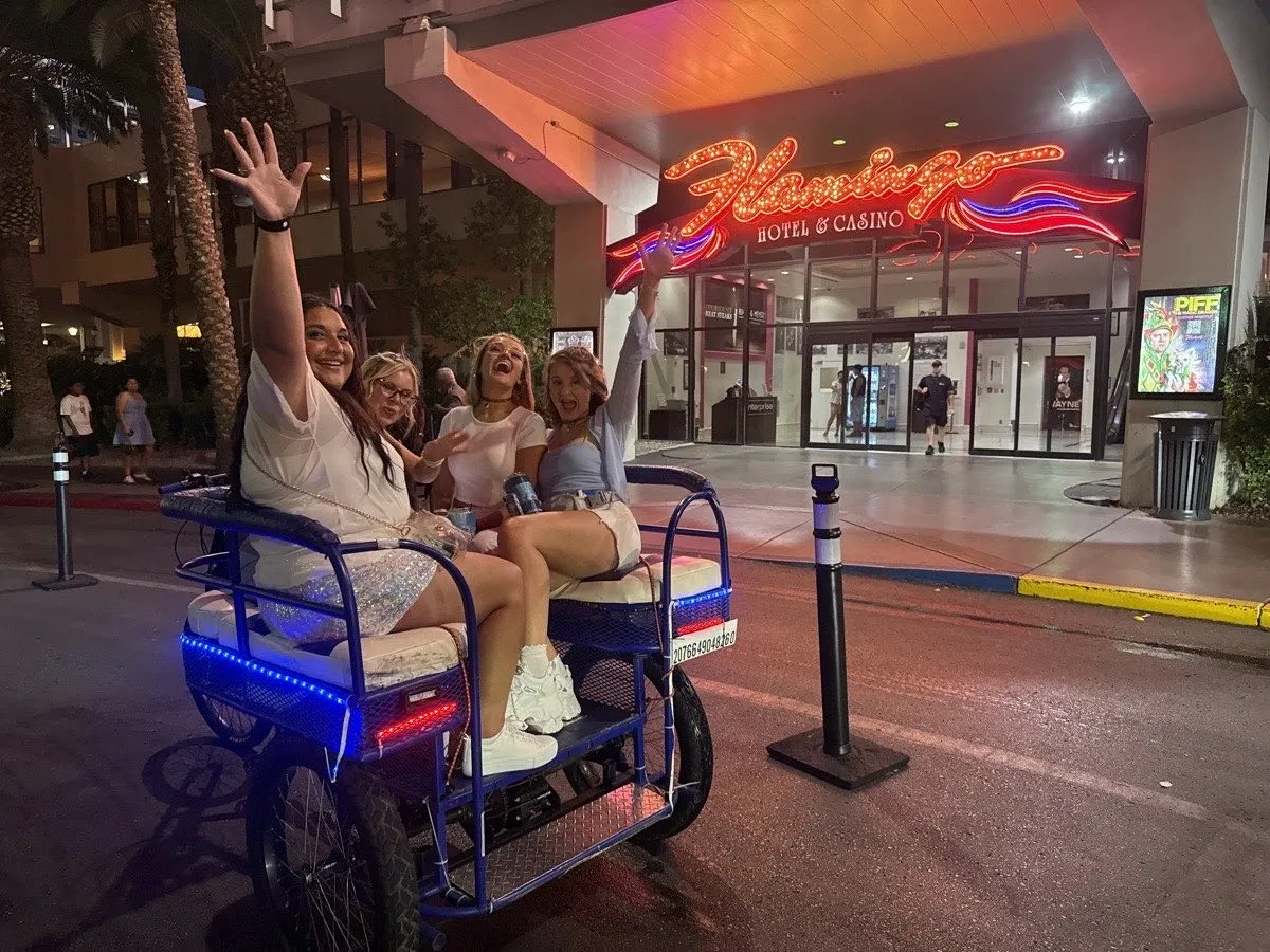 Group of riders cheering in a Vegas Bike Cab pedicab under the Flamingo neon sign on the Las Vegas Strip