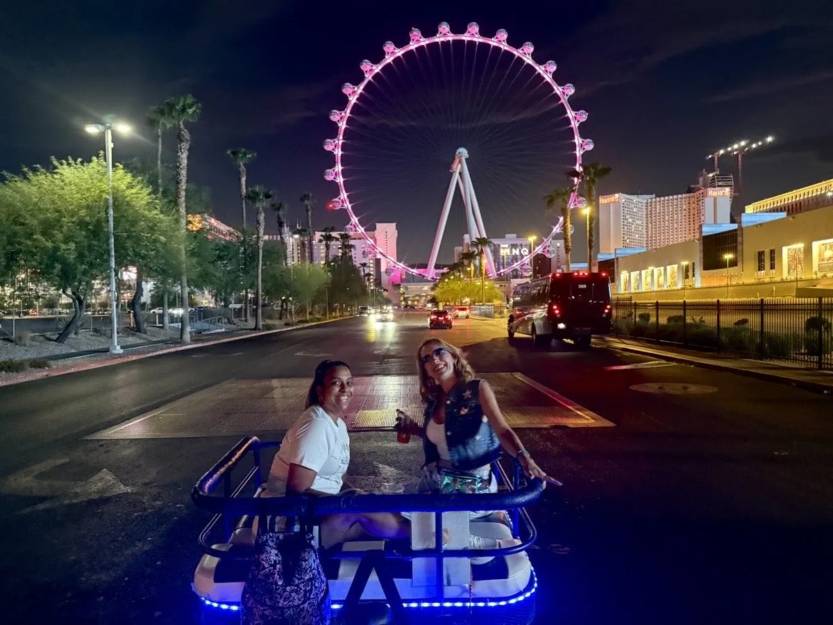 Two Vegas Bike Cab riders in a lit pedicab at night beneath the High Roller observation wheel